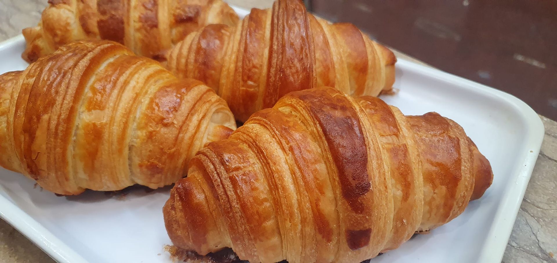 Cuatro croissants dorados y hojaldrados reposan sobre una bandeja rectangular blanca.