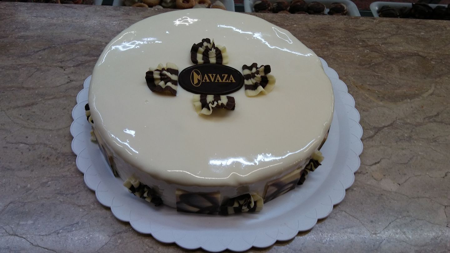 Un pastel redondo glaseado en blanco con adornos de chocolate y el logotipo de 