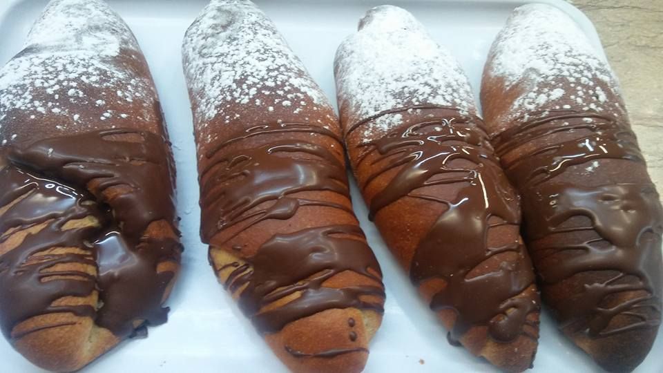 Cuatro pasteles dorados, bañados en glaseado de chocolate y espolvoreados con azúcar glas, dispuestos en una bandeja blanca.