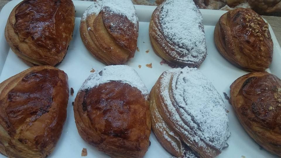 Una bandeja con ocho hojaldres dorados y doblados, algunos espolvoreados con azúcar glas, dispuestos en dos filas.