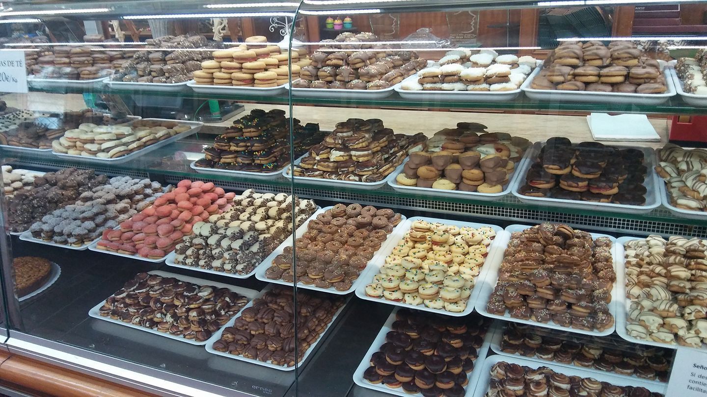 Vitrinas de cristal llenas de galletas y pasteles variados, dispuestos en bandejas en una panadería.
