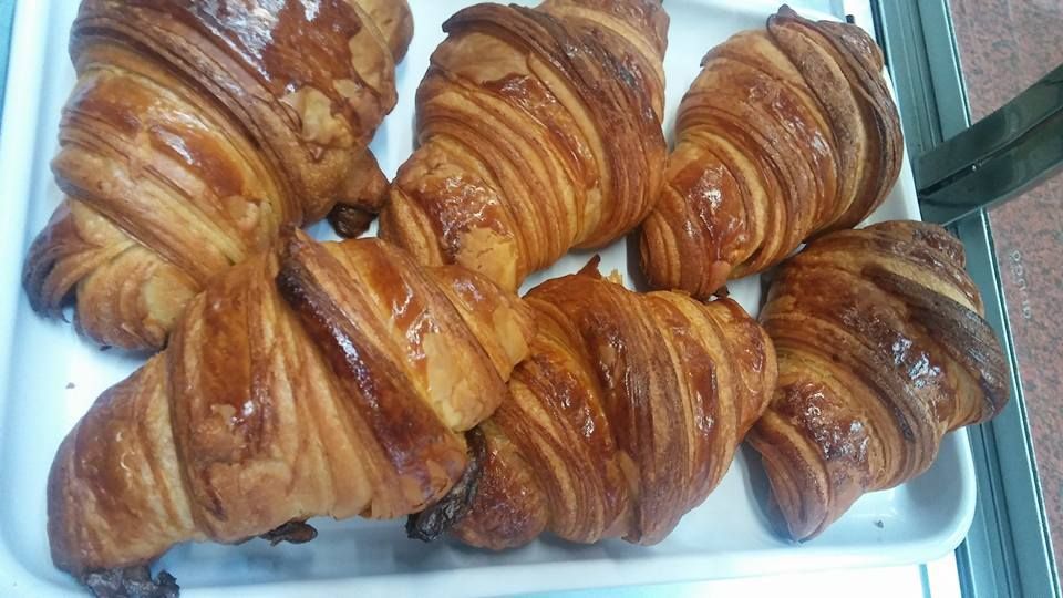 Una bandeja blanca con cinco croissants dorados, hojaldrados y en forma de media luna, dispuestos muy juntos.