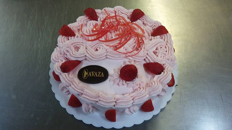 Un pastel redondo con glaseado rosa, decorado con fresas, adornos rojos y una placa de chocolate con la inscripción