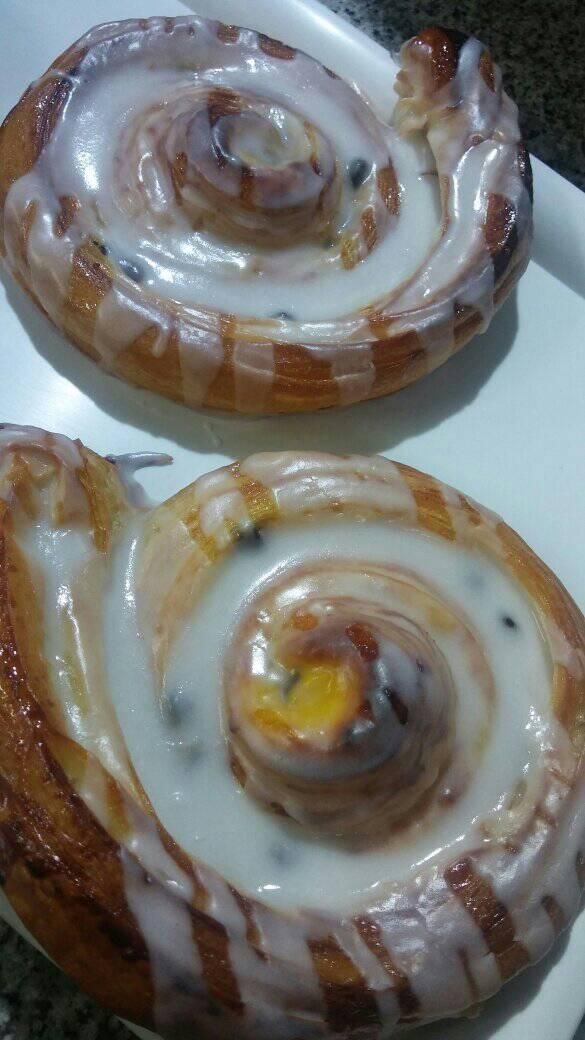 Dos pasteles daneses dorados en forma de espiral, glaseados con crema blanca y salpicados de trocitos de chocolate negro.