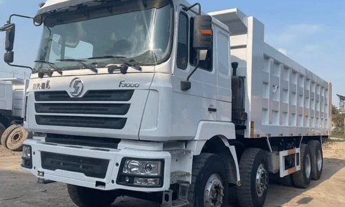 A white dump truck is parked in a dirt field.