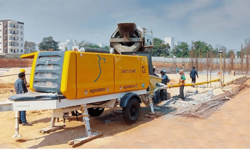 A yellow concrete pump is on a trailer at a construction site.