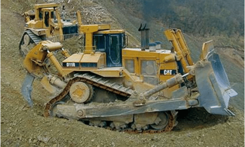 A cat bulldozer is sitting on top of a dirt hill