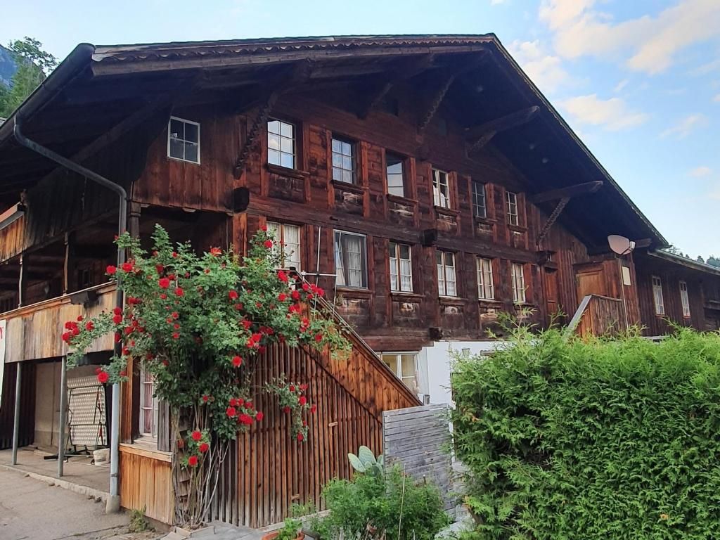 Rustic wooden chalet with red flowers and green shrubs under a partly cloudy sky
