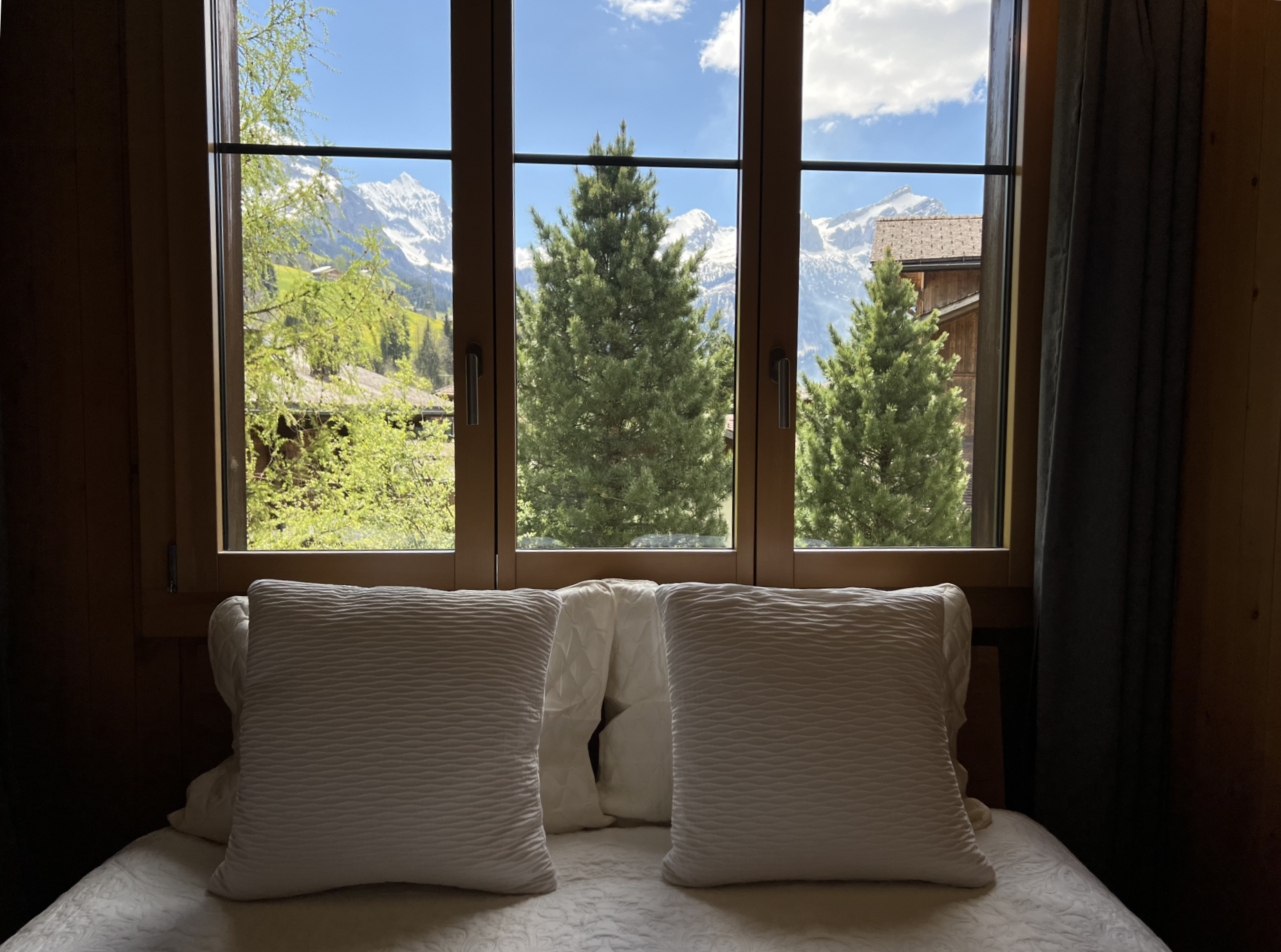 A bed with white pillows and a window with a view of the mountains.