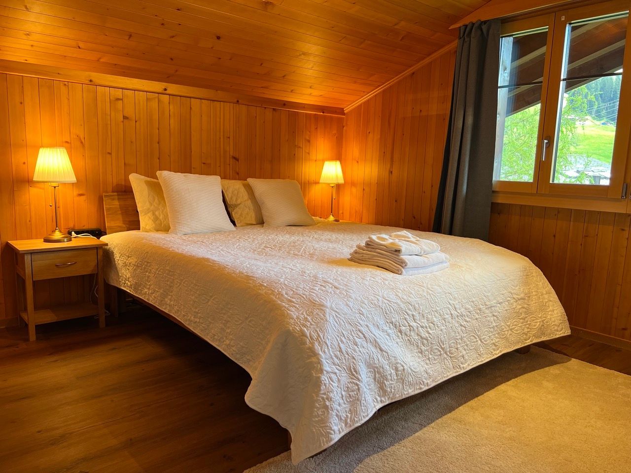 A bedroom with a bed , nightstand , lamps and a window.