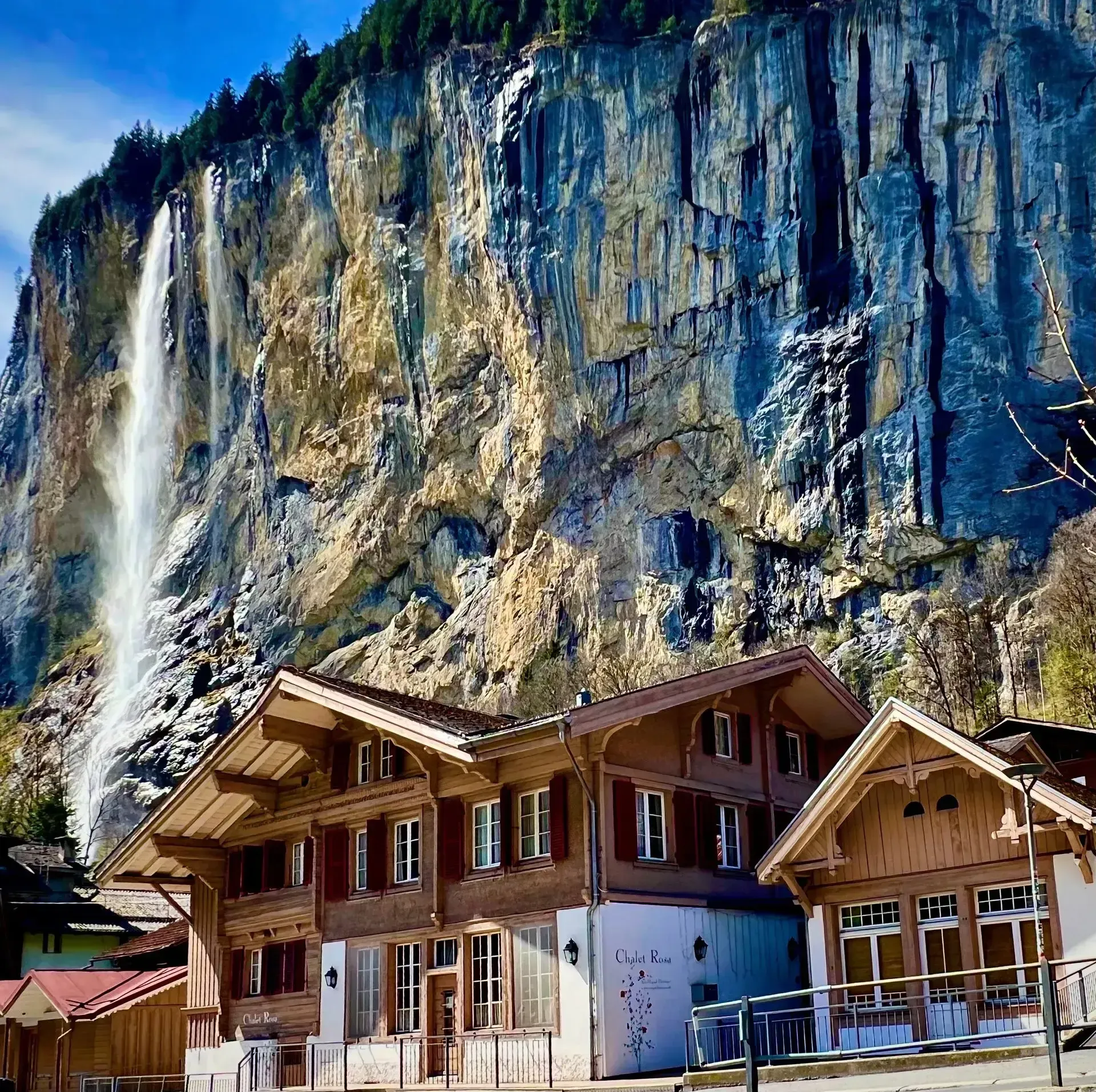 Wooden chalets at the base of a steep rocky cliff under a clear blue sky