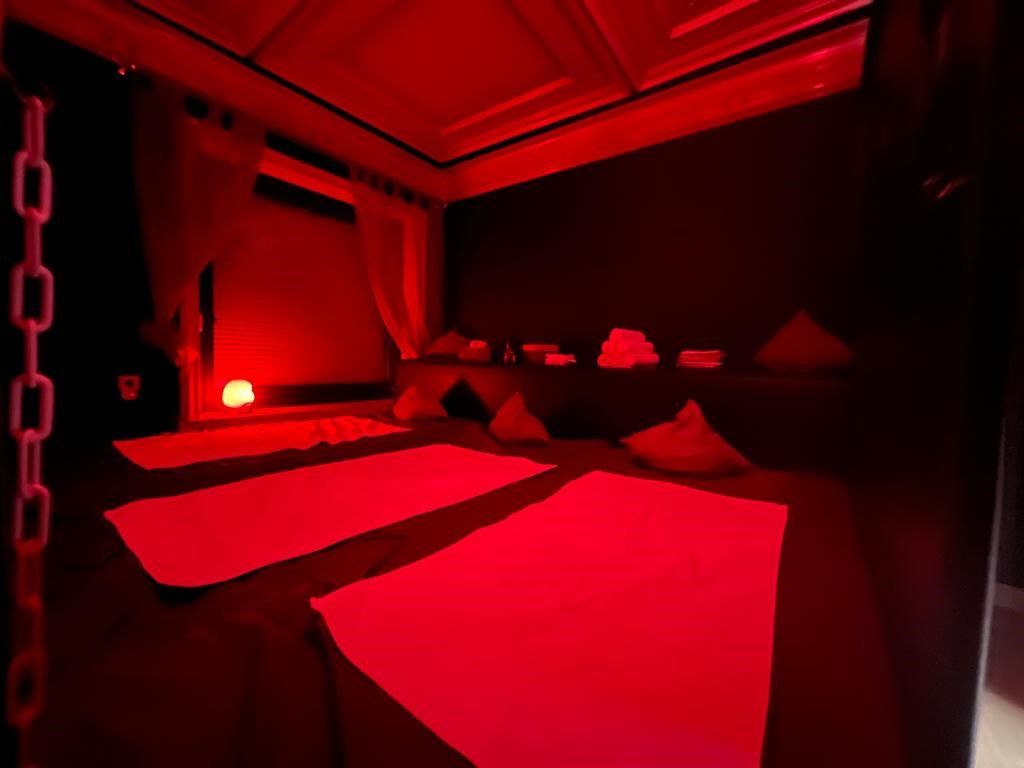 Ein rot beleuchteter Meditationsraum mit auf dem Boden ausgelegten Matten und Kissen. Links hängt eine Kette.