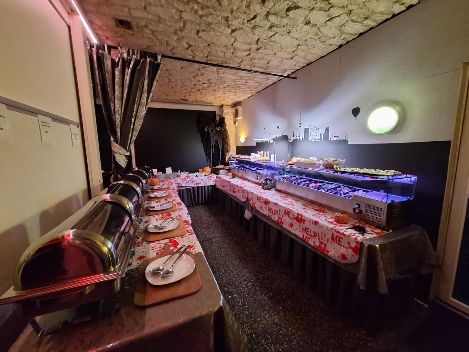 Buffet mit verschiedenen Speisenbehältern, Tellern und Besteck in schwach beleuchteter Umgebung.