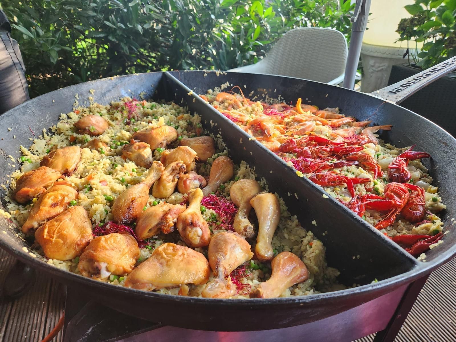 Große Paellapfanne, unterteilt in zwei Bereiche: Hühnercouscous und Garnelen mit roter Paprika. Im Freien.