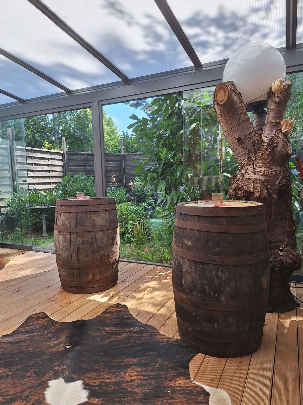 Zwei verwitterte Holzfässer im Innenbereich, daneben ein großer dekorativer Baumstamm, der eine weiße Kugel trägt.