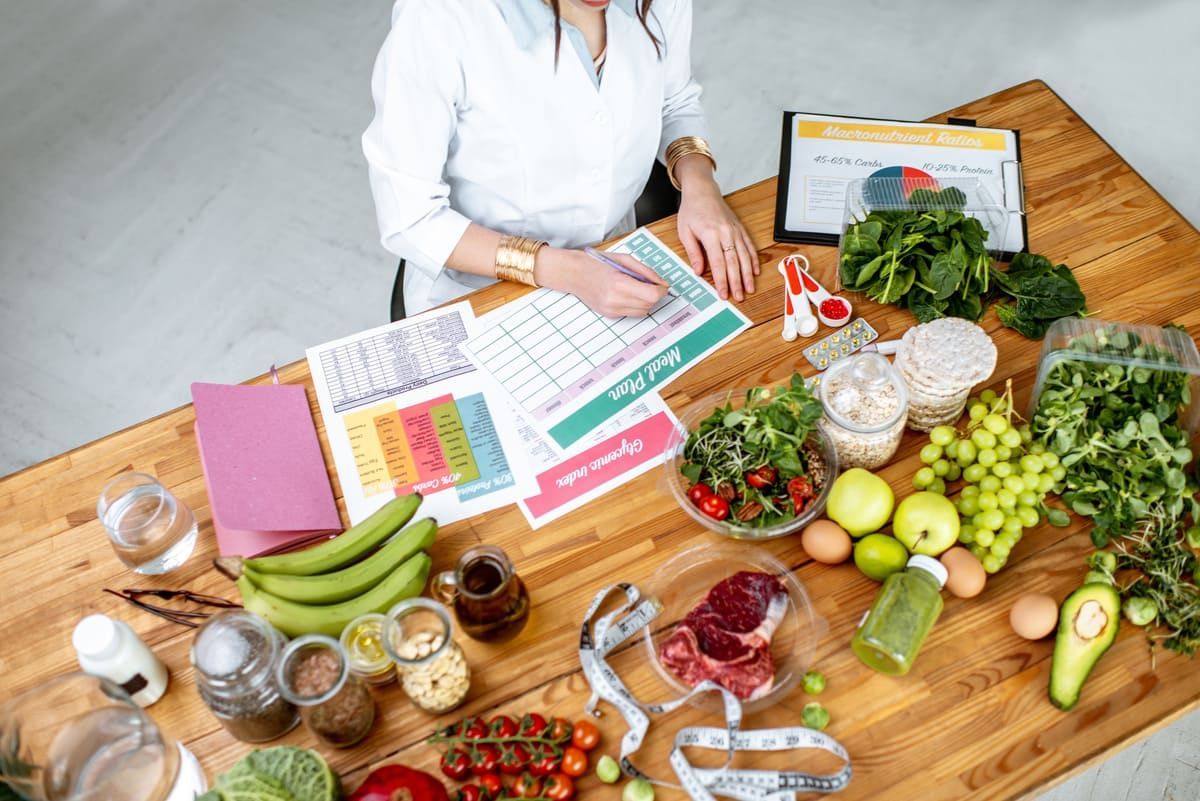 Una mujer está sentada en una mesa rodeada de frutas y verduras.
