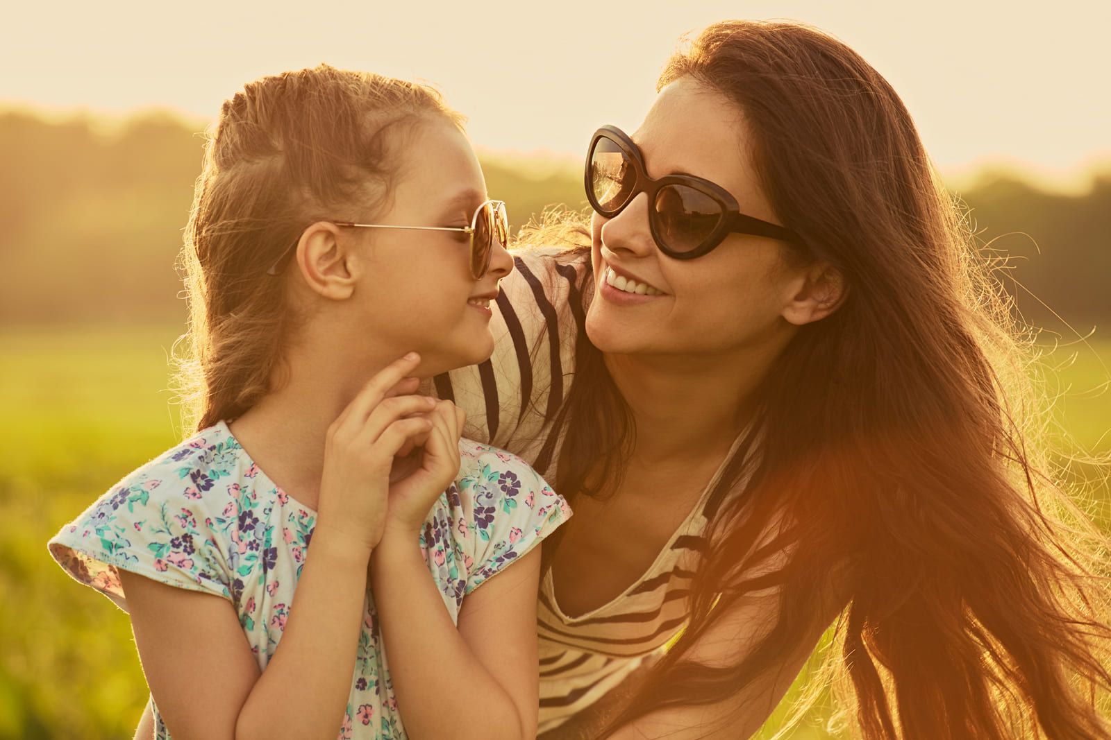 Una mujer y una niña que llevan gafas de sol se miran en un campo.