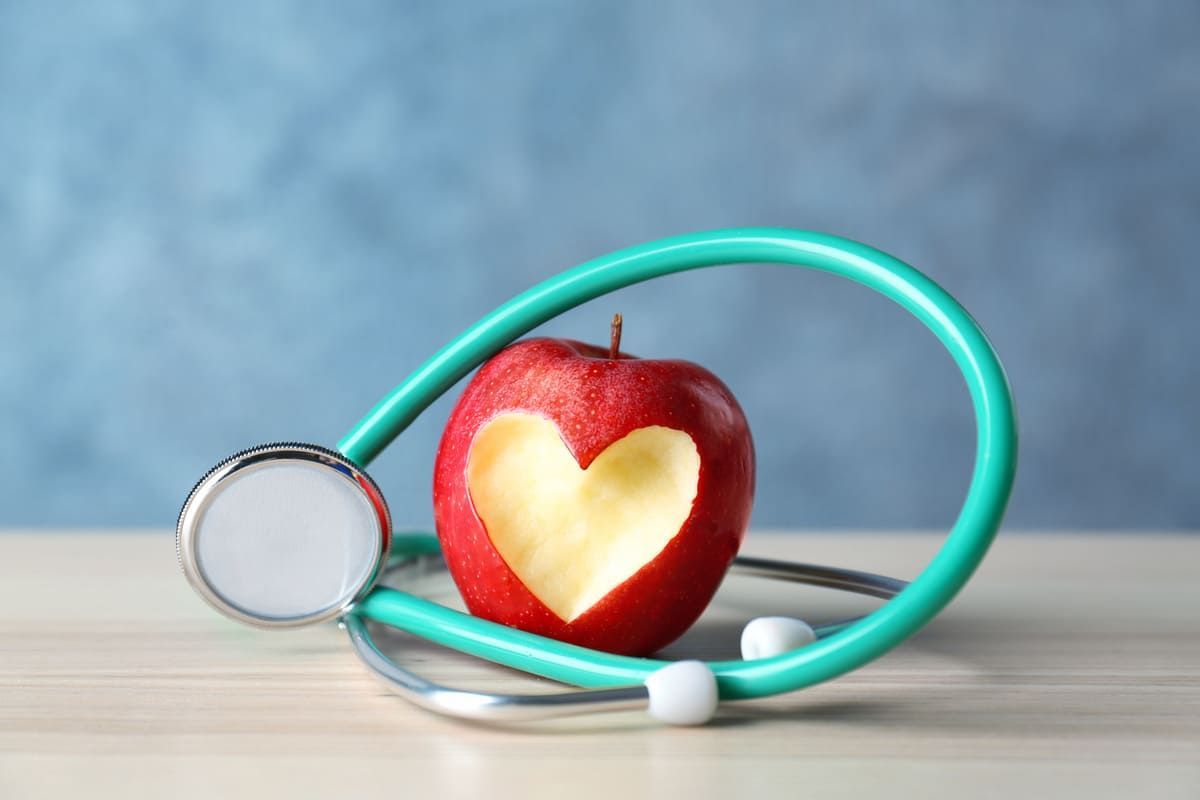 Una manzana con un corazón cortado y un estetoscopio alrededor.