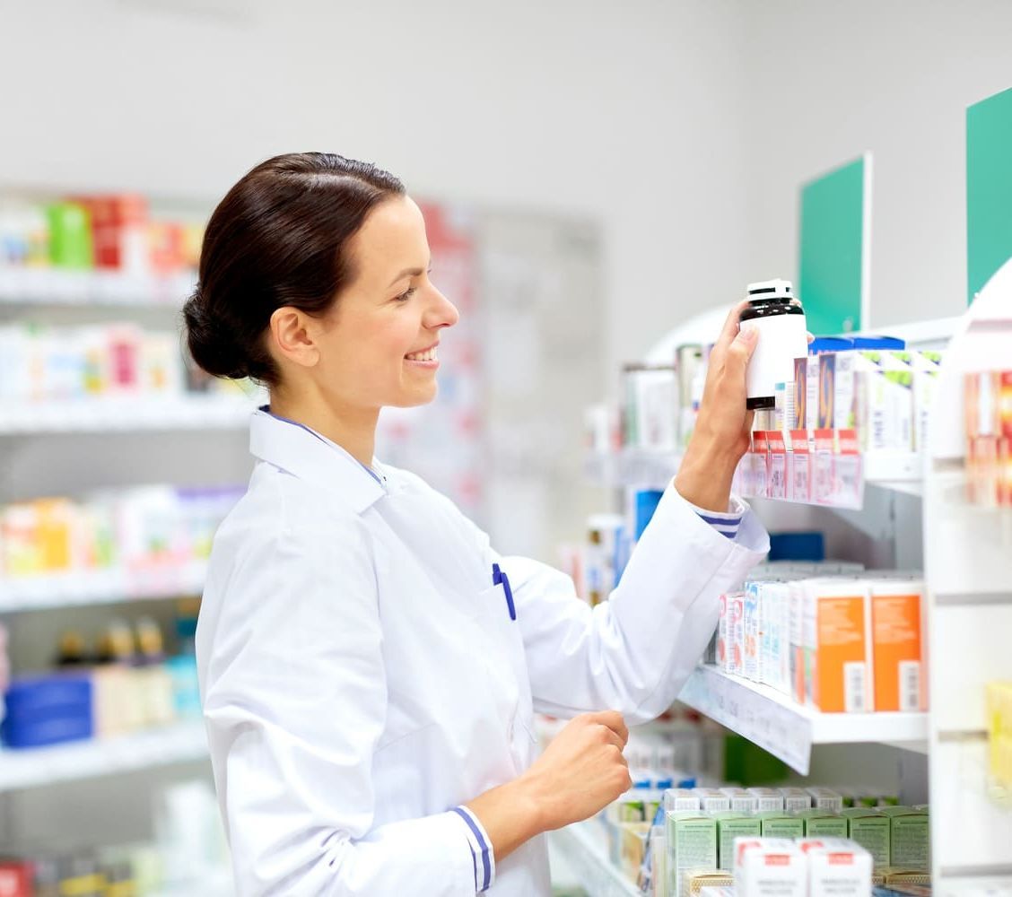 Una farmacéutica está mirando un frasco de medicamentos en una farmacia.