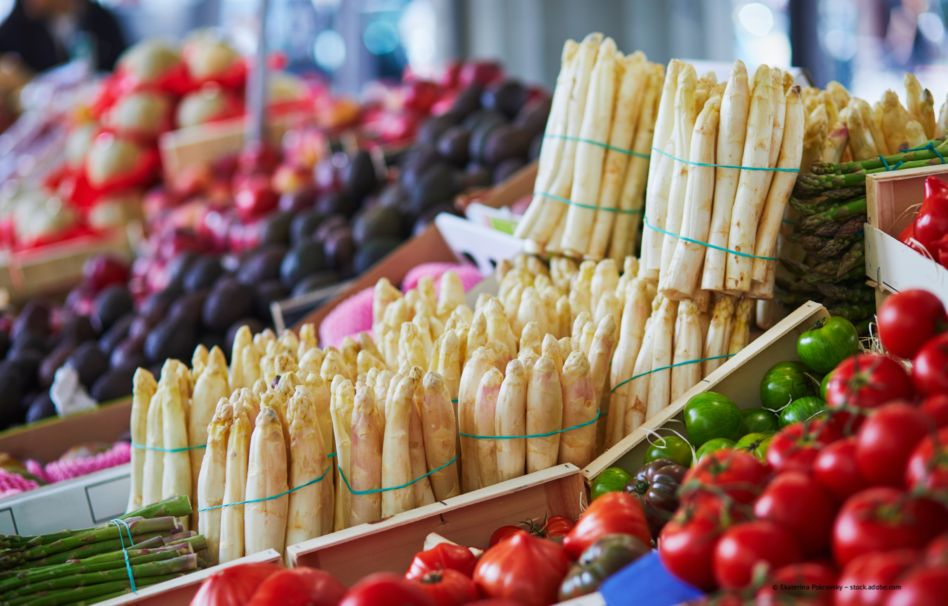 Marktstand mit Bündeln von weißem Spargel und roten Tomaten in bunten Gemüsekisten