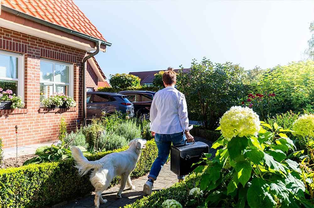 Eine Frau geht mit einem Hund und einem Koffer vor einem Backsteinhaus spazieren .