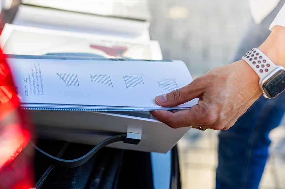 Ein Mann hält ein Buch in der Hand , während er neben einem Auto steht .