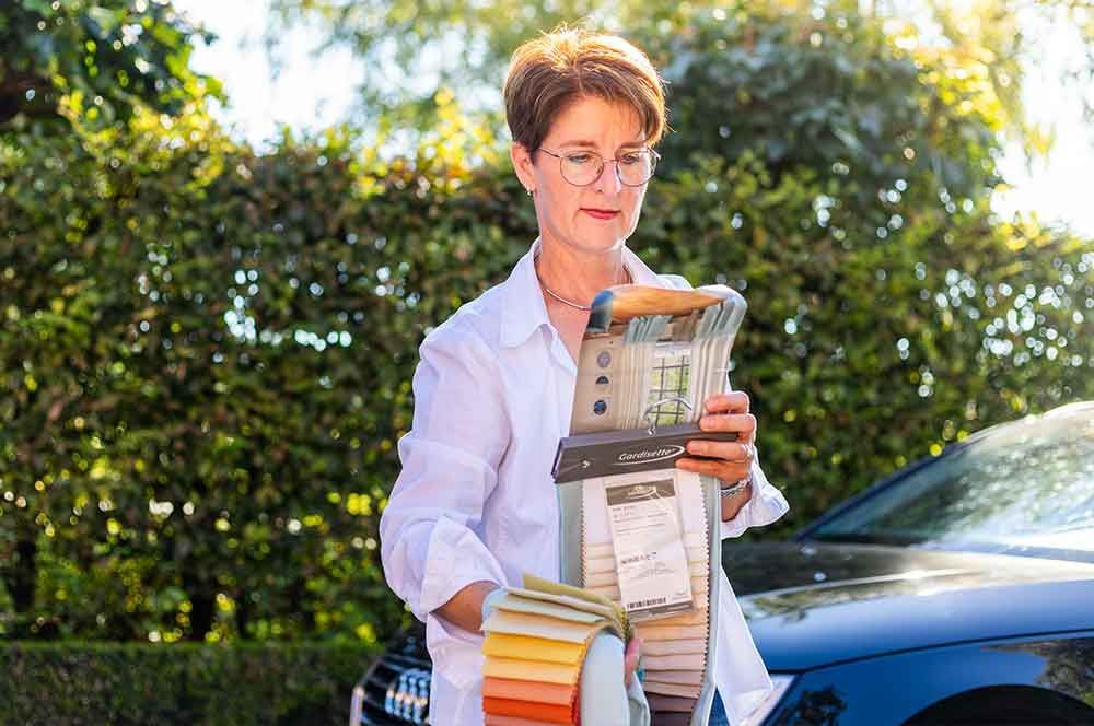 Eine Frau hält eine Auswahl an Stoffen vor einem Auto .