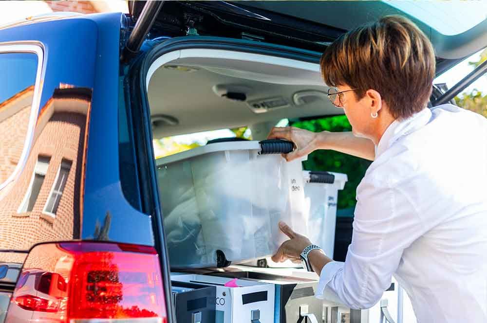 Eine Frau nimmt einen Plastikbehälter aus dem Kofferraum eines Autos .