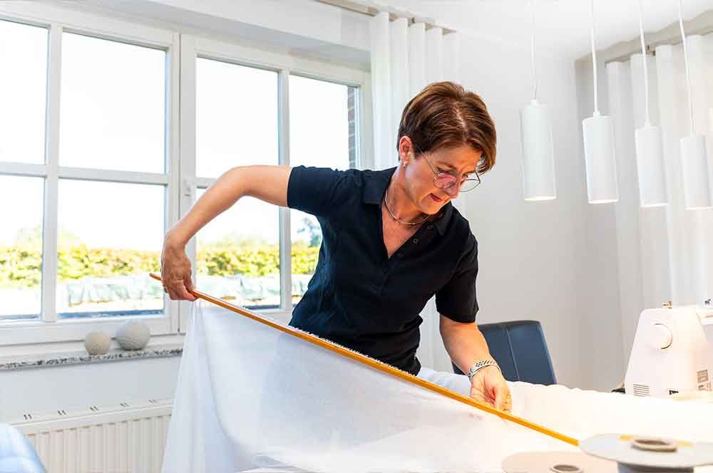 Eine Frau steht an einem Tisch und misst etwas mit einem Lineal .