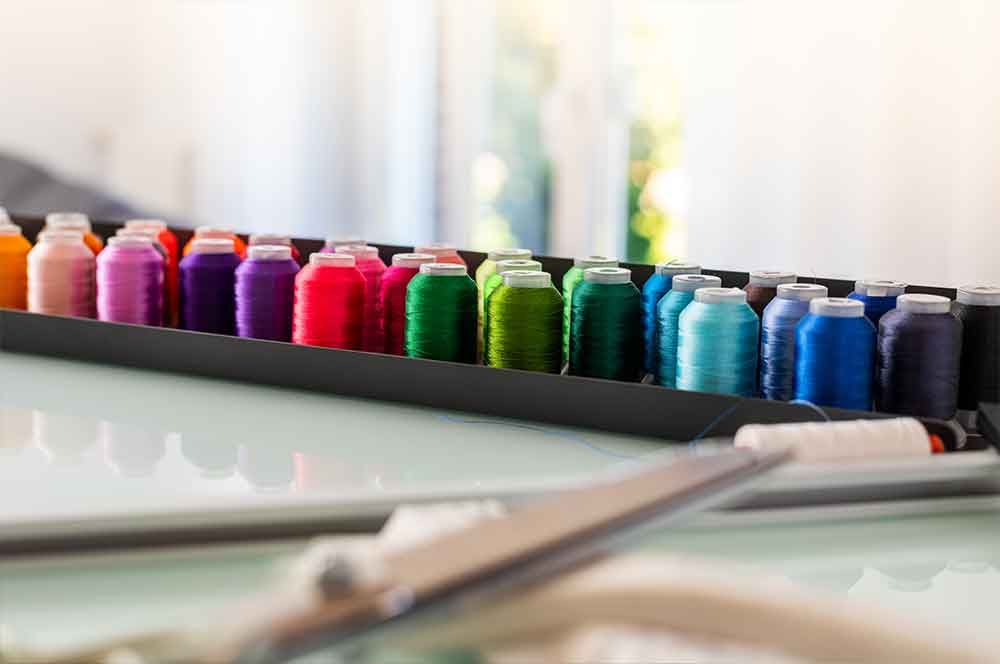 Auf einem Tisch steht eine Schachtel mit bunten Garnspulen und einer Schere .