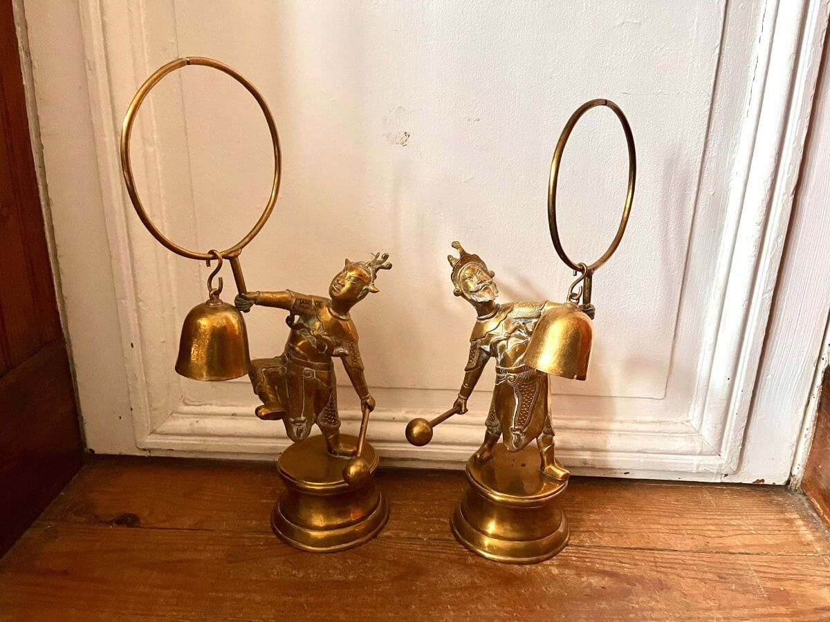 Deux statues en laiton ornées de personnages tenant des cloches et des cerceaux.