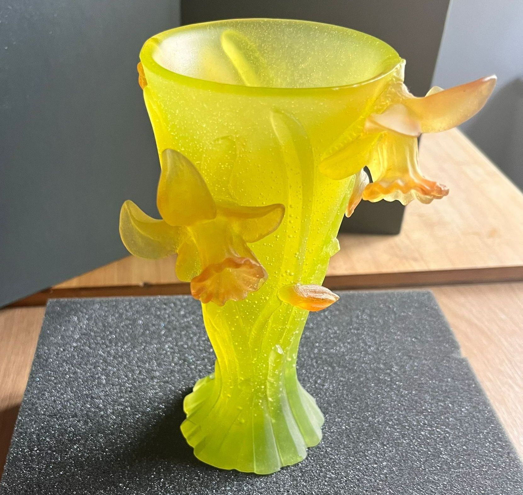 Vase en verre jaune avec des fleurs de jonquilles, sur une surface en mousse grise.