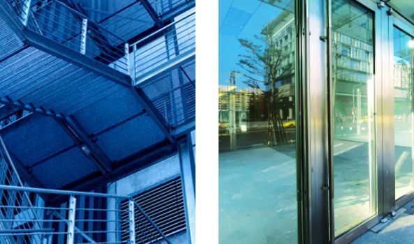 Escalera de cristal tintado de azul junto a la entrada de un moderno edificio de cristal con reflejos.