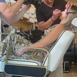 Una mujer está sentada en una silla mientras un hombre la maquilla.