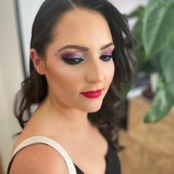 Una mujer lleva sombra de ojos morada y lápiz labial rojo.