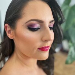 Un primer plano del rostro de una mujer con sombra de ojos violeta y lápiz labial rojo.