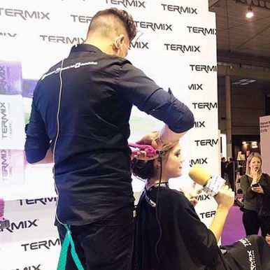 Un hombre está trabajando en el cabello de una mujer frente a un cartel que dice Termix