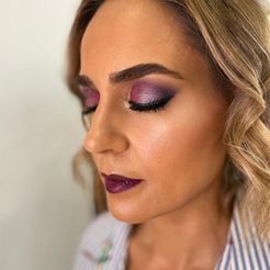 Una mujer con sombra de ojos violeta y lápiz labial violeta lleva una camisa a rayas.