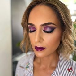 Una mujer con sombra de ojos violeta y lápiz labial violeta lleva una camisa a rayas.