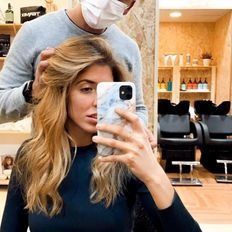 Una mujer se toma un selfie en una peluquería mientras un hombre le sostiene el cabello.