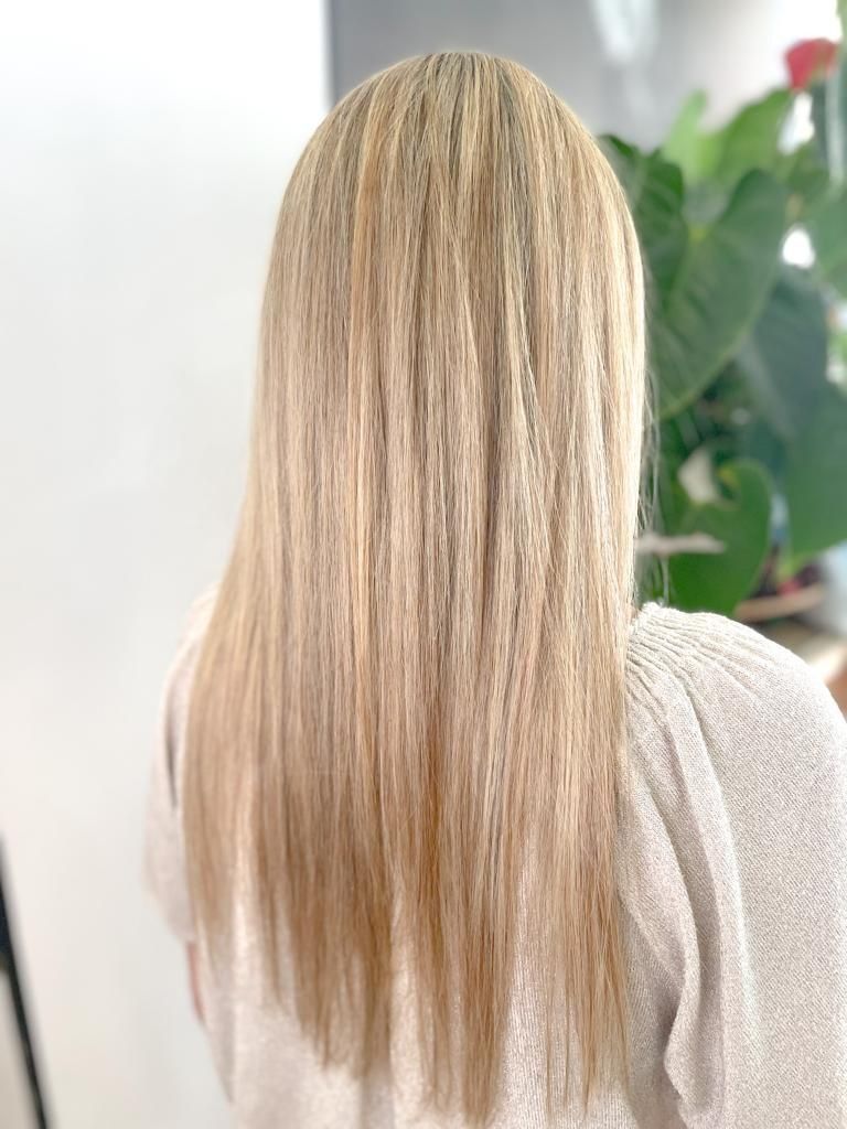 Una mujer con cabello largo y rubio está sentada frente a una planta.