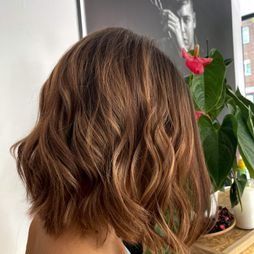 Una mujer con cabello corto y castaño está parada frente a una planta.