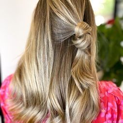 Una mujer con cabello largo y rubio lleva un vestido rosa y tiene el cabello recogido en una cola de caballo mitad arriba y mitad abajo.
