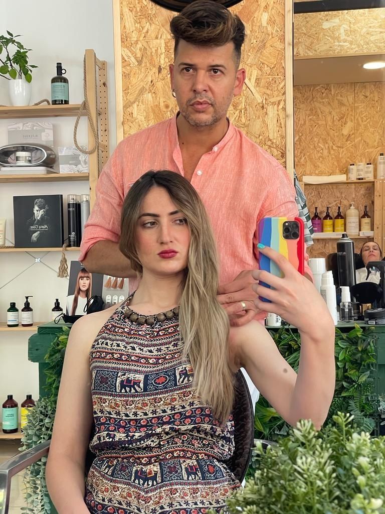 Una mujer está sentada en una silla mientras un hombre le sostiene el cabello.