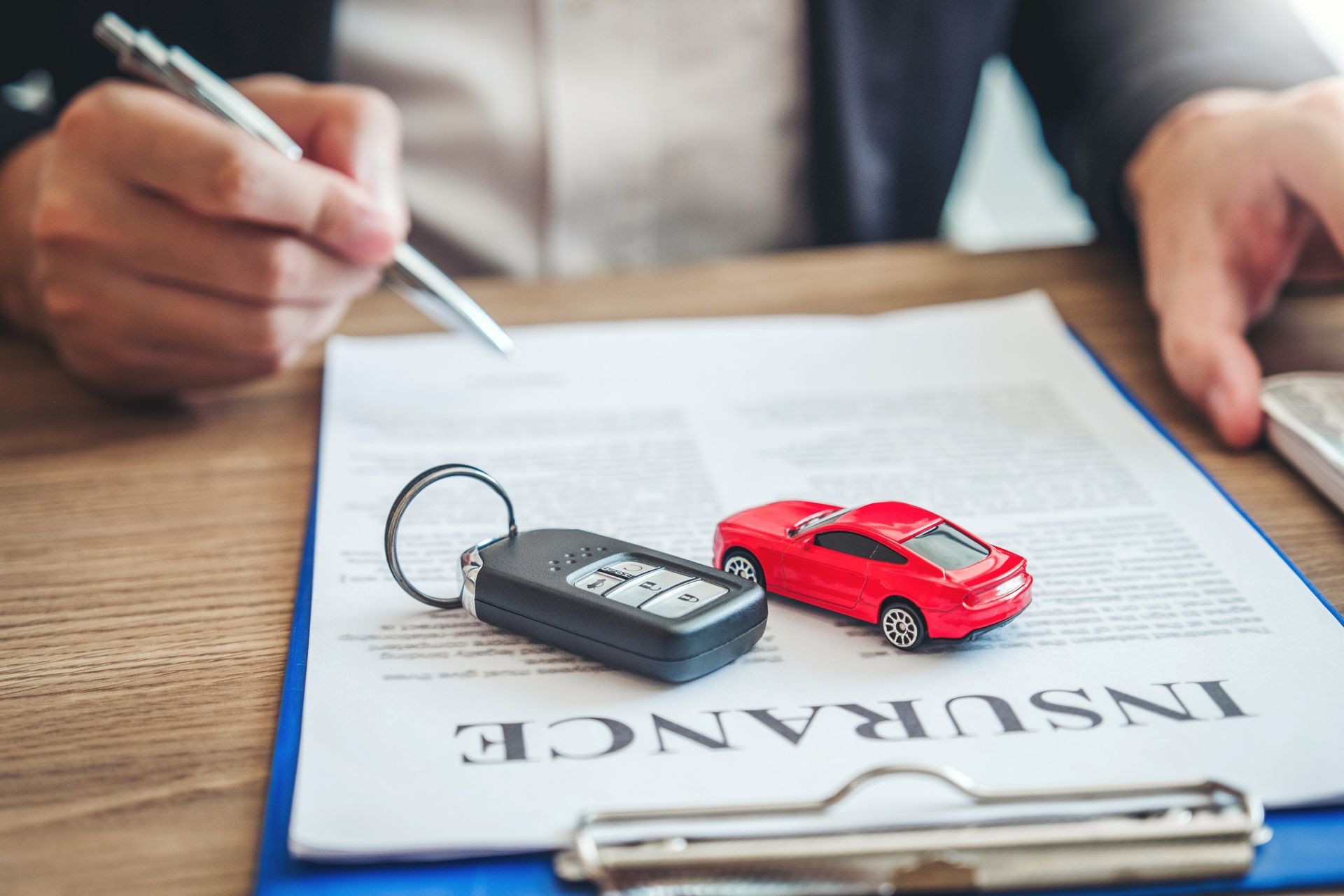 Un hombre está escribiendo en un portapapeles al lado de un coche de juguete y una llave de coche.