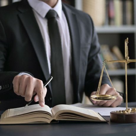 Un hombre con traje y corbata está sentado en un escritorio sosteniendo un bolígrafo y un libro.