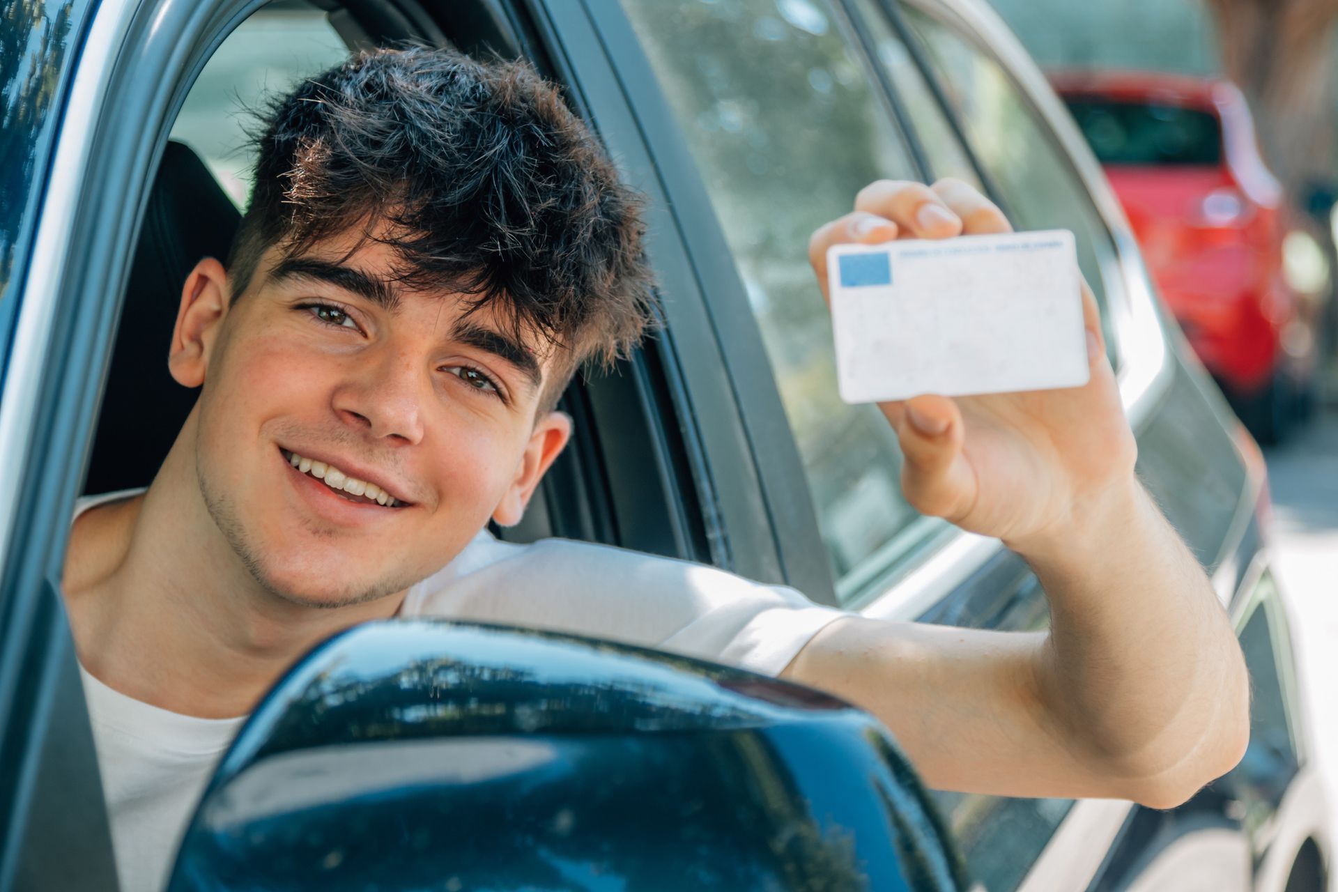 Un joven está sentado en un coche con un permiso de conducir en la mano.