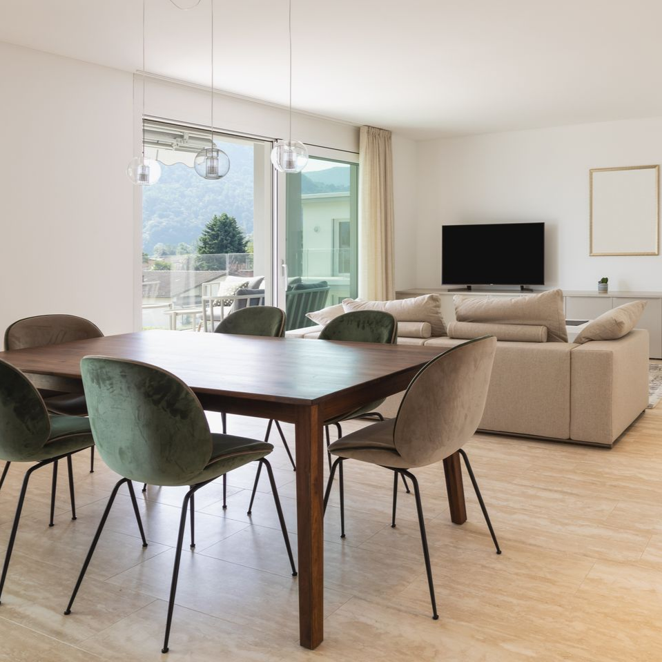 Salle à manger et salon modernes avec une table en bois, des chaises vertes, un canapé beige, une télévision et une grande baie vitrée.