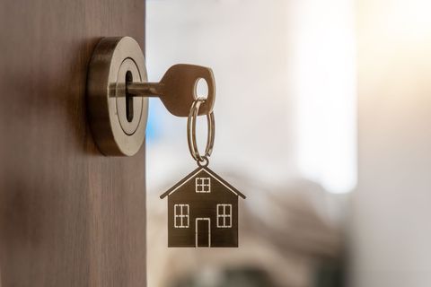 Un porte-clés avec un pendentif en forme de maison ; clé insérée dans une serrure de porte.