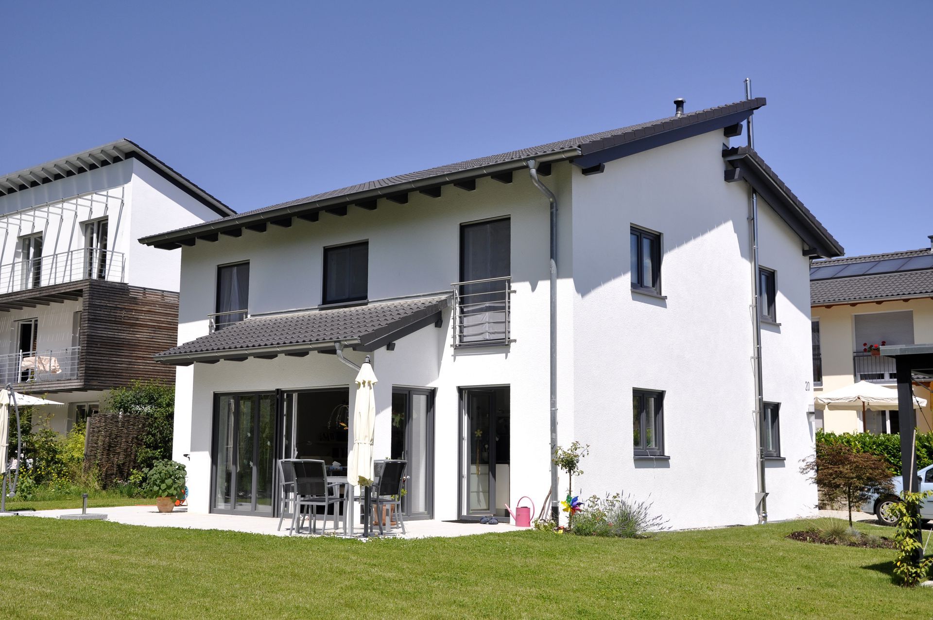 Maison individuelle moderne à deux étages avec façade blanche, grandes baies vitrées et jardin arboré.